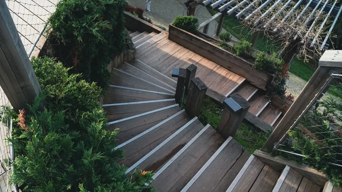 Tarima de madera exterior en forma de escalinata, vista desde arriba, rodeada de vegetación de jardín.