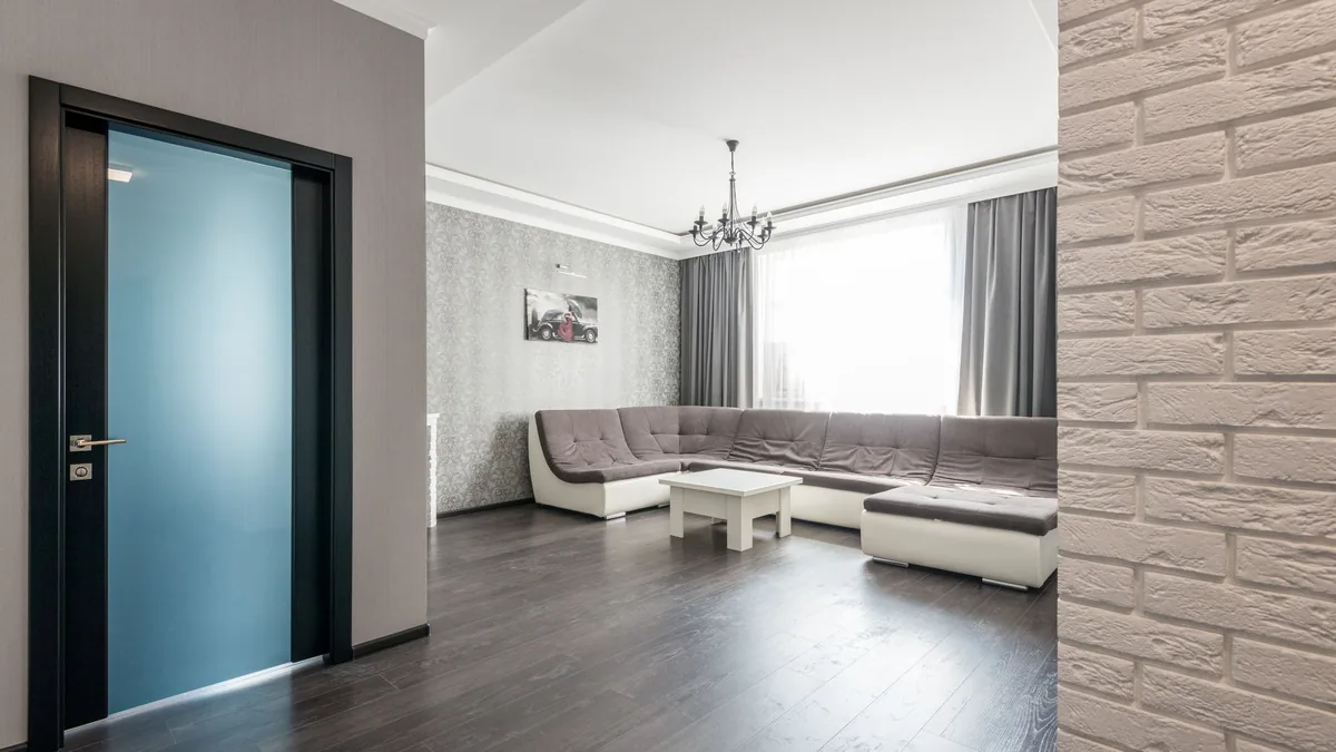 Salón con suelo de lamas en tono nogal oscuro, sofá gris y una pared de ladrillo visto como acento decorativo.