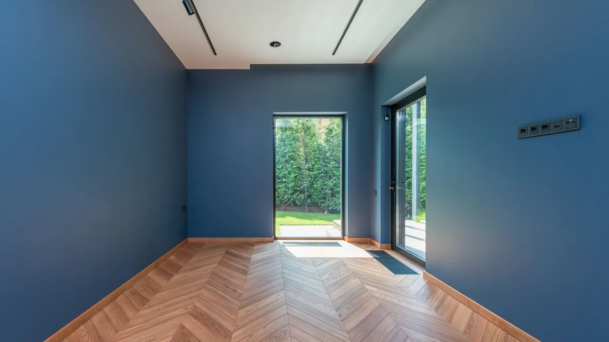 Suelo de parquet en espiga junto a una puerta acristalada que da a un jardín, en una habitación de paredes azules.